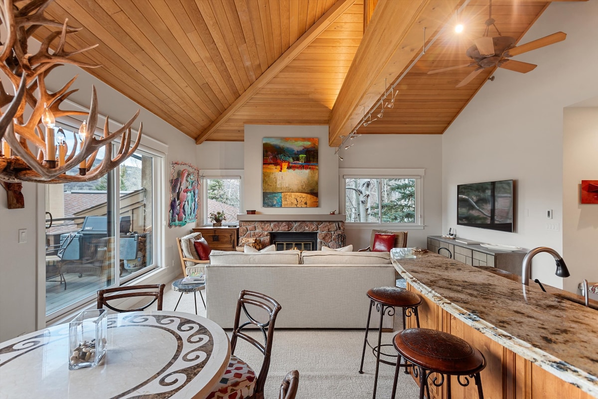 Open concept Snowmass condo living room with vaulted ceiling, fireplace, dining area, and kitchen